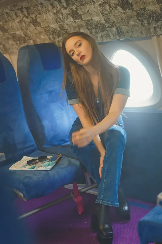 Paola sur un siège bleu de la cabine, combinaison en jean