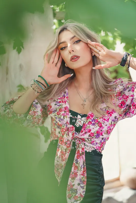 Anaïs en blouse fleurie sous la véranda envahie par la vigne