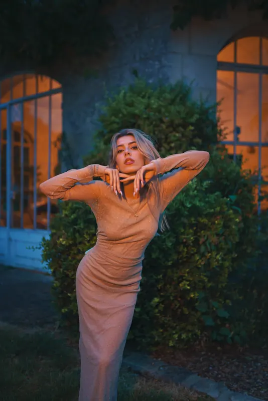 Anaïs bras levés devant les fenêtres cintrées éclairées, au petit matin