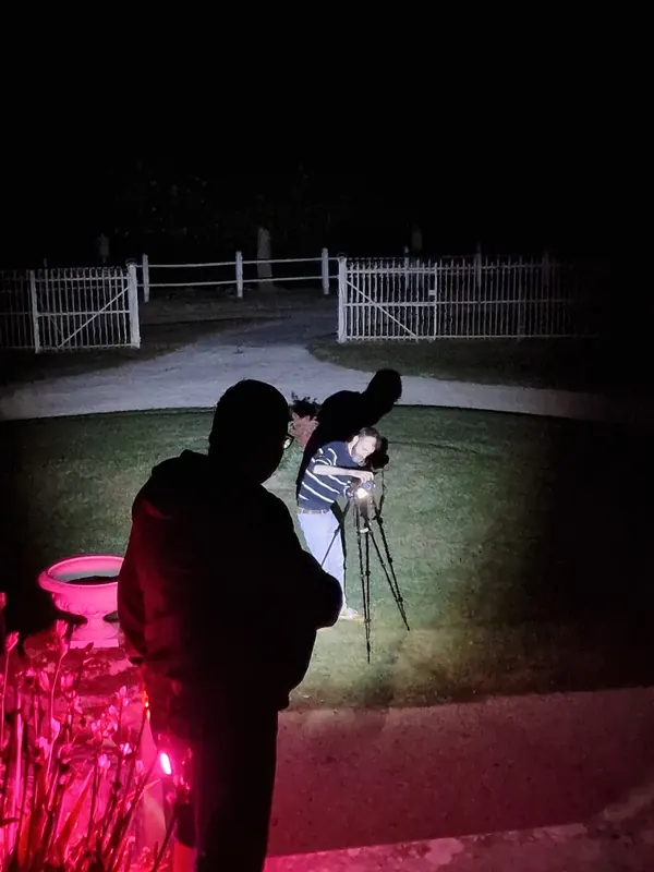 Un photographe et son trépied dans la nuit, éclairé en rose