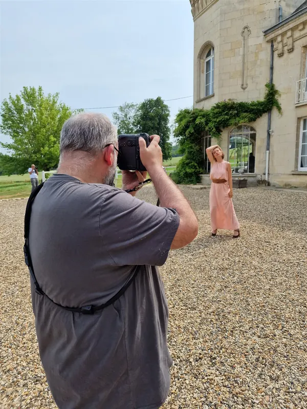 Un photographe en action devant la façade, une modèle en robe rose dans la cour