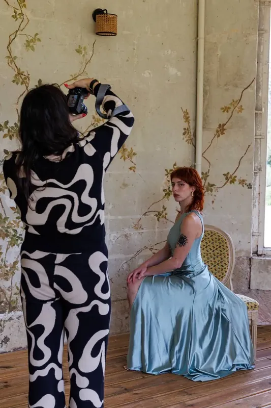 Une photographe dirige une modèle en robe bleue devant les murs peints du salon