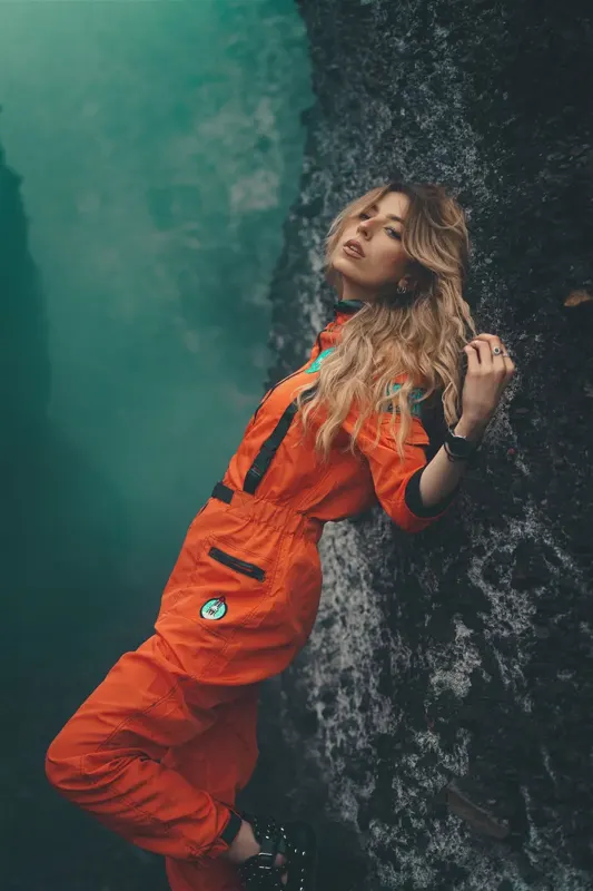Anaïs en combinaison orange adossée au schiste, fumée bleu-vert