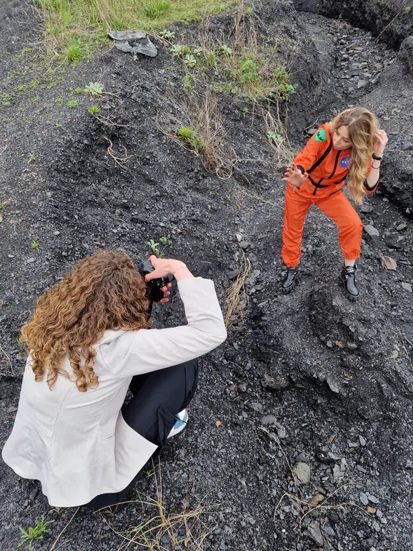 Valentine accroupie photographie Anaïs en combinaison orange sur la pente du terril