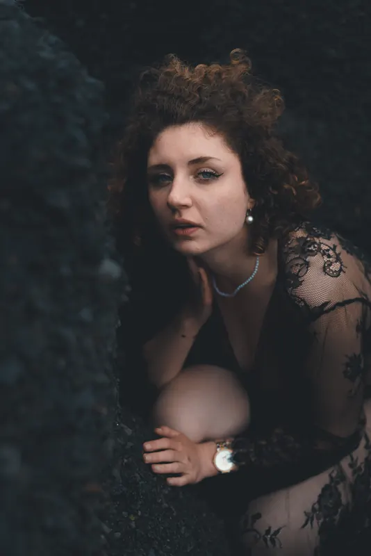 Valentine en dentelle noire, regard vers l’objectif, adossée à la roche noire